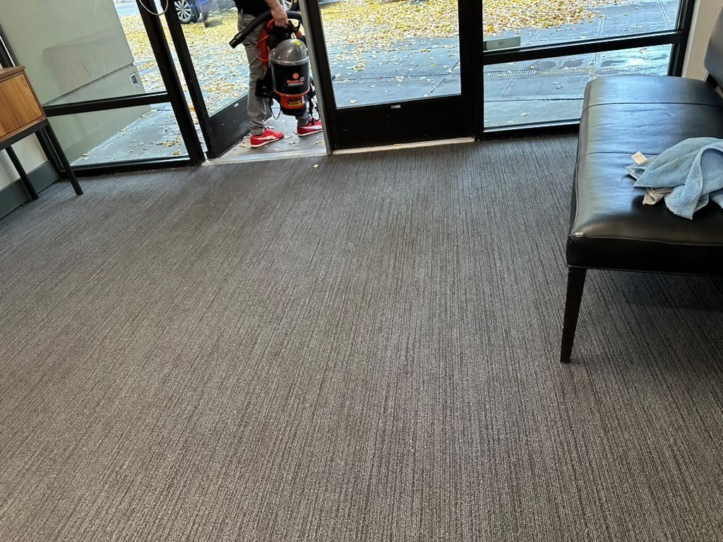 Freshly vacuumed commercial lobby carpet with a technician using a backpack vacuum